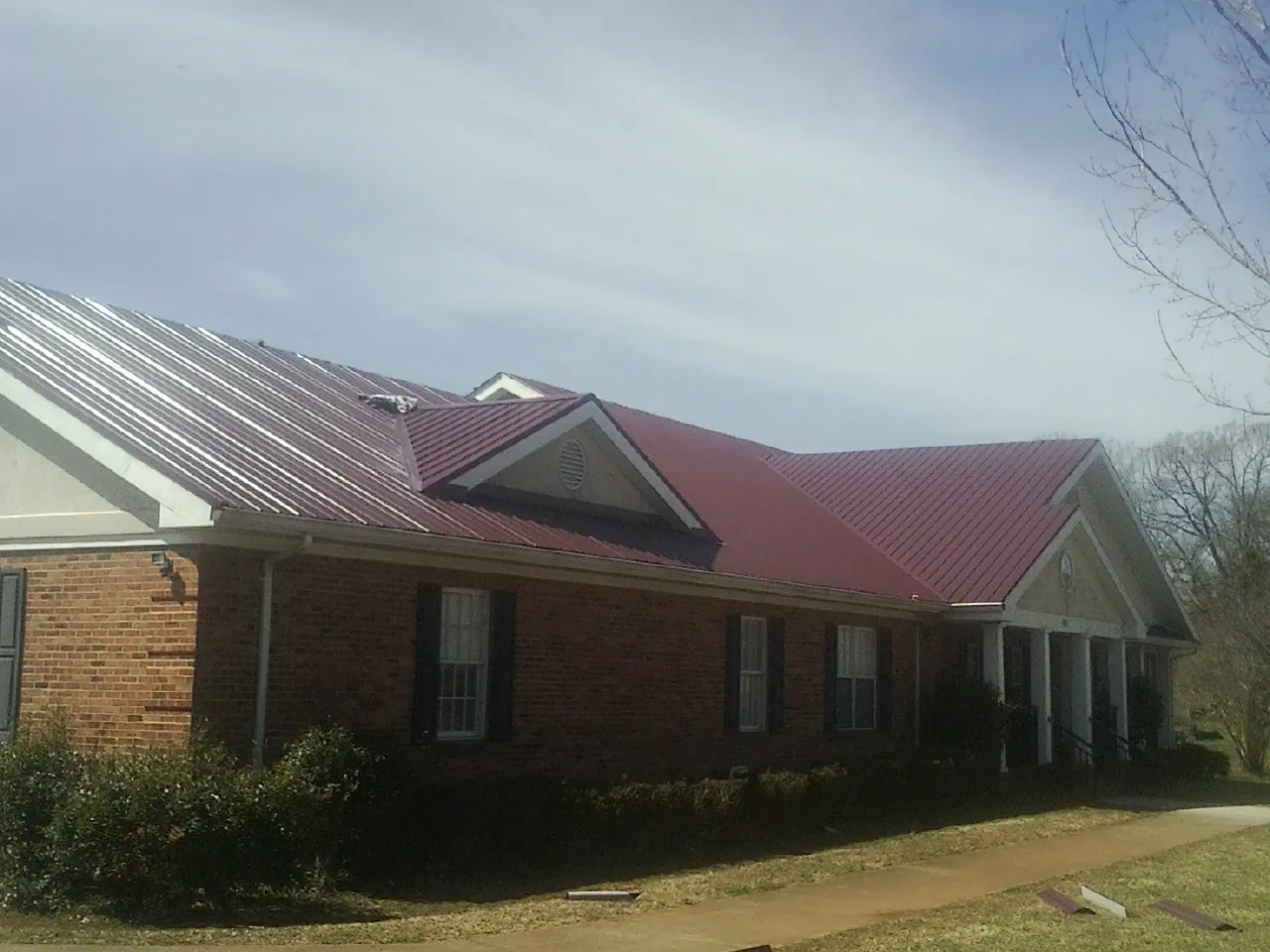 Red metal roof with gabled entries on a long brick building, from a Hail Damage Roof Repair job in Smithton
