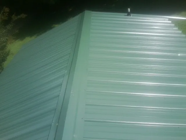 New green metal panels meeting at the ridge of a roof — Flat Roof Repair work by our crew in Smithton