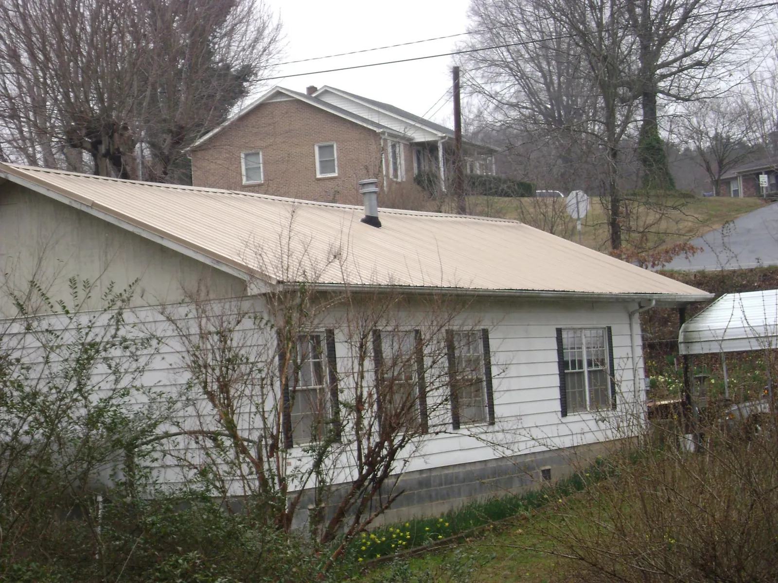 Tan metal roof on a white sided house set into a hillside — Commercial Roofing by Roofing Brothers in Smithton